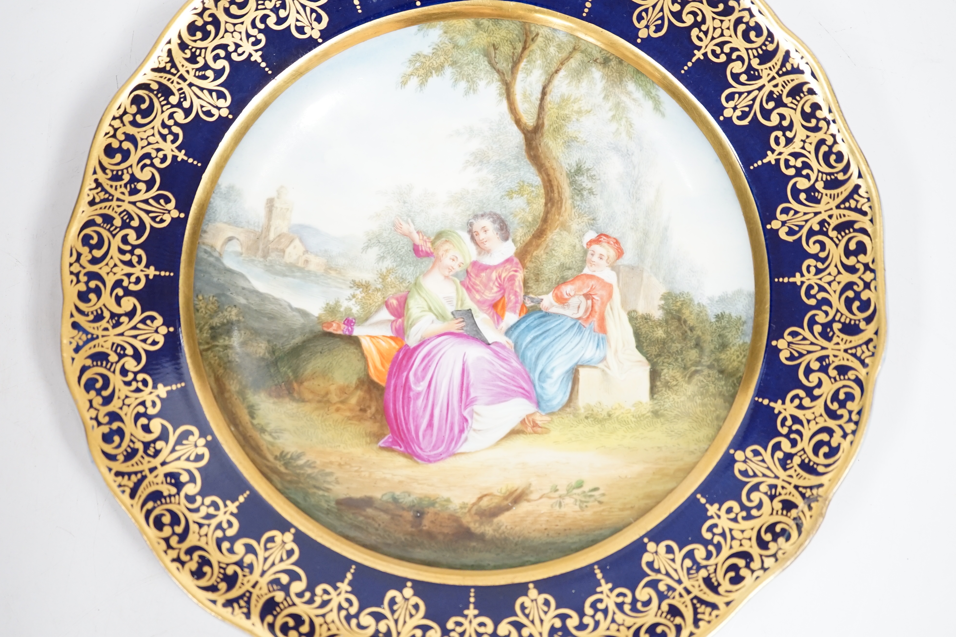 A Meissen-style rich blue and gilt bordered dish, the centre painted with a romantic scene with figures